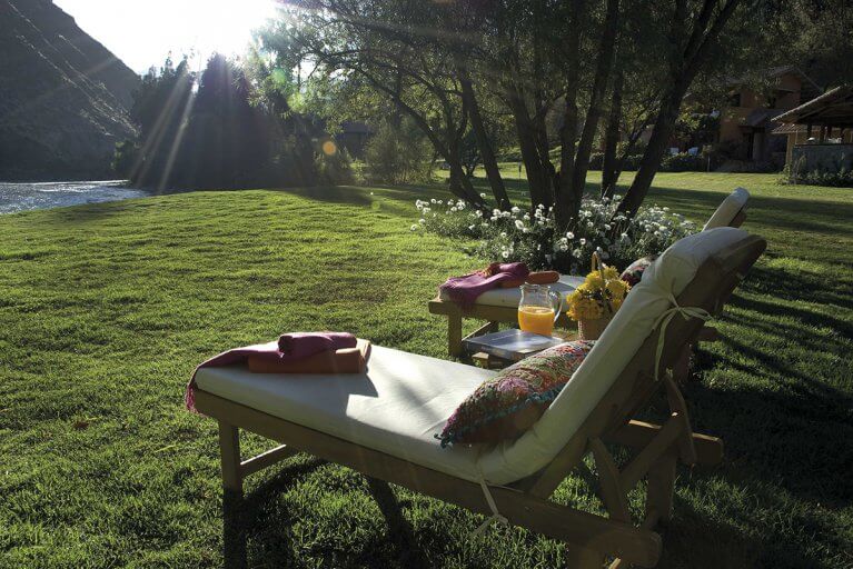 Lounge chairs with cushions and side table near the river at the Belmond Hotel Rio Sagrado