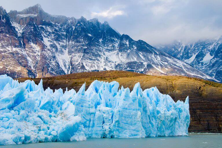 Icy blue glacier and lake in front of snowy mountains in Torres del Paine, Patagonia