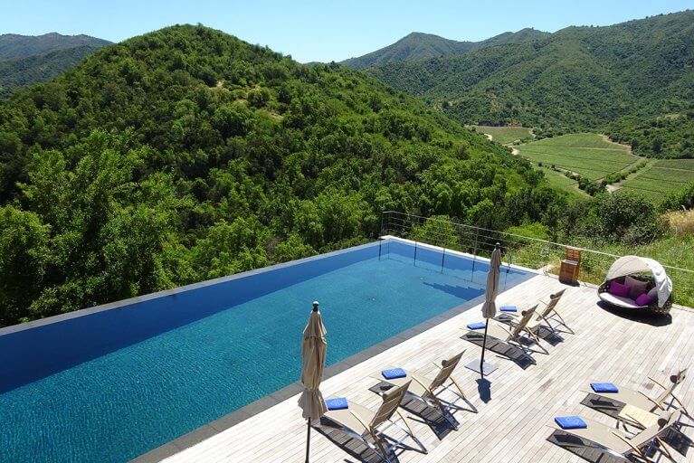 Outdoor pool with a large deck and view of green mountains at Viña Vik hotel in Chile