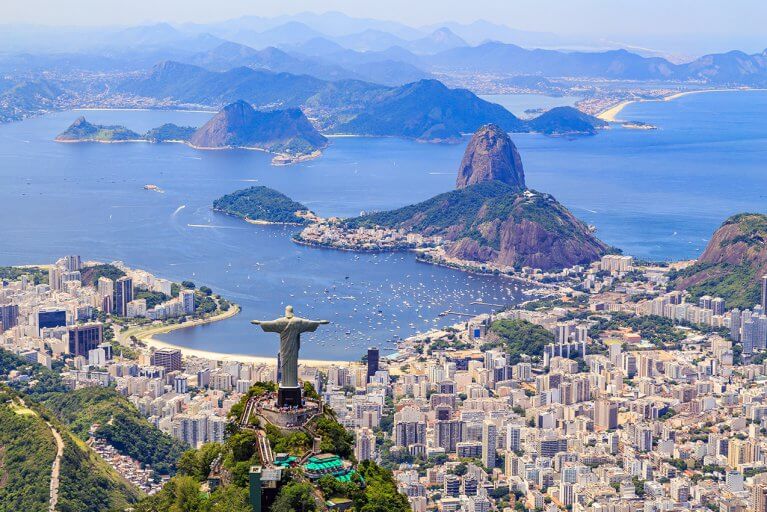 Looking down at back of Christ the Redeemer, buildings of Rio de Janeiro, mountains, and bay