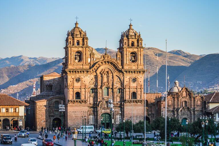 Cathedral in Cusco's busy main square at sunset with mountains behind