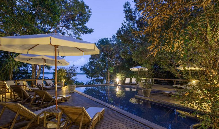 Deck with sun loungers and umbrellas around outdoor pool with view of Amazon River at Anavilhanas Lodge in evening