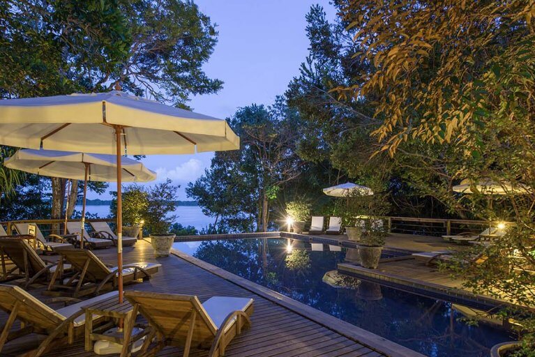 Deck with sun loungers and umbrellas around outdoor pool with view of Amazon River at Anavilhanas Lodge in evening