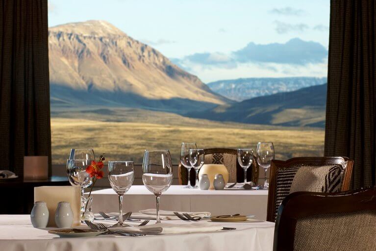 Tables set for dinner in the dining room at Eolo Hotel with a view of mountains out the window during a luxury Patagonia tour