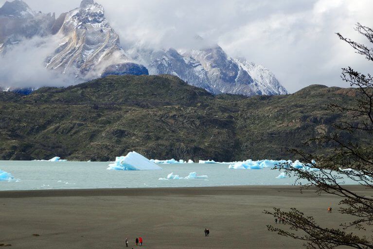 Travelers admiring a glacial lake with floating icebergs in front of mountains during a luxury Patagonia tour