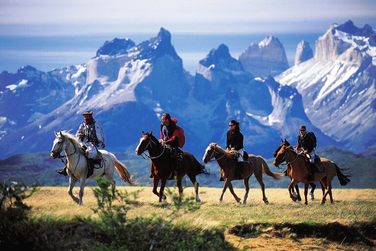 Four people horseback riding through a field in front of mountains on a luxury private tour in Torres del Paine, Patagonia