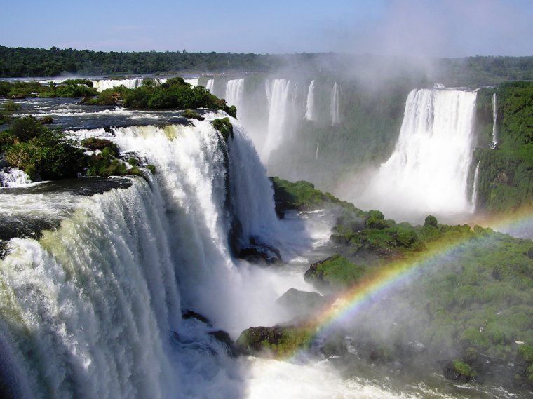 Water flowing over the edge of Iguazu Falls creating a rainbow and mist