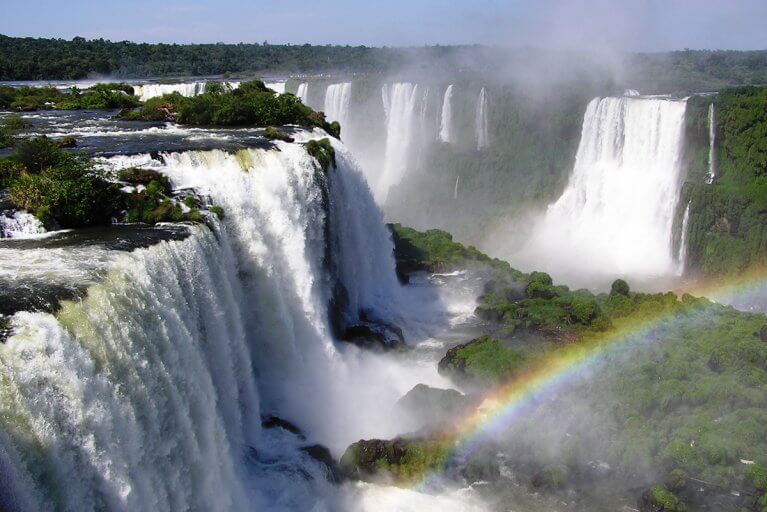 Water flowing over the edge of Iguazu Falls creating a rainbow and mist