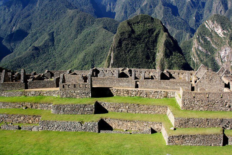 Stone terraces with grass and houses without roofs at Machu Picchu with the green Andes mountains in the background