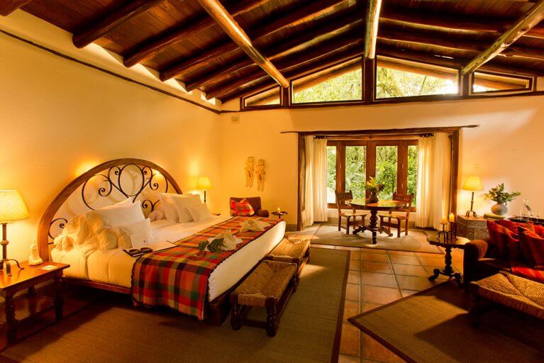 Spacious, luxury suite at Inkaterra Hotel with a large bed, traditional Peruvian decor, and exposed wooden beams on ceiling