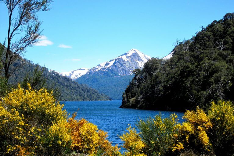 Villa-style hotel called Villa Beluno with red roofs by a lake and surrounded by forest with mountains in the distance