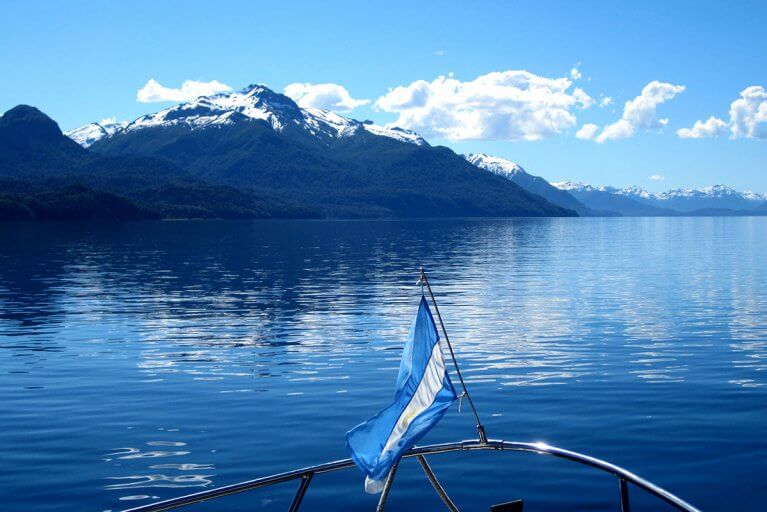 Argentinian flag on the bow of a boat on a lake in Patagonia with snow capped mountains in the distance