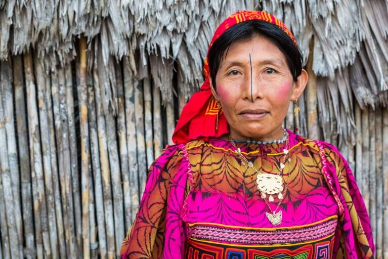 Close up portrait of a Guna lady in traditional colourful robes in front of a hut in the San Blas Islands