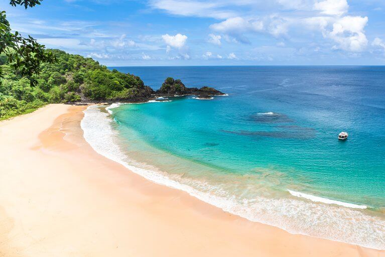 Looking down at the pristine sands of Praia do Sancho with small boat anchored nearby in the sea in Fernando de Noronha