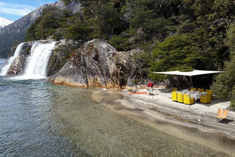 Private gourmet picnic set up on the shore of Isla Victoria near a waterfall in Argentina's Lake District
