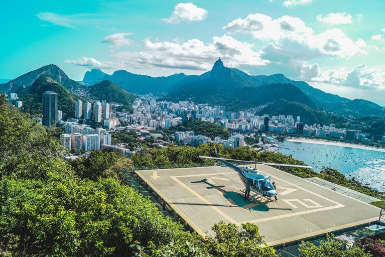 Helicopter taking off from helipad with cityscape of Rio de Janeiro and mountains in background during luxury tour of Brazil
