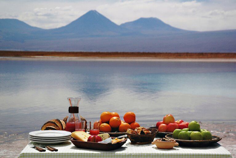 Private picnic with fruit, cheese, and bread set up by a lake in the Atacama Desert during a private tour of Chile