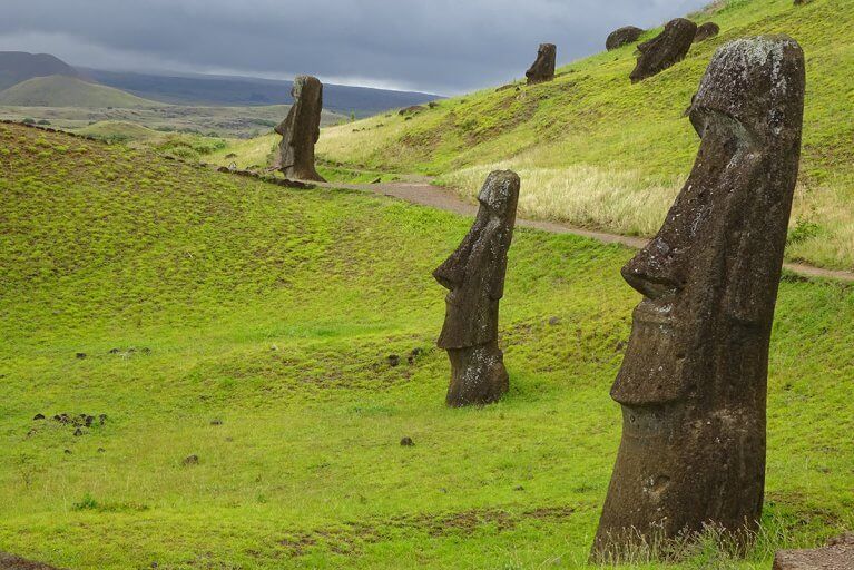 Five Moai statues seen from side on a green hill on Easter Island