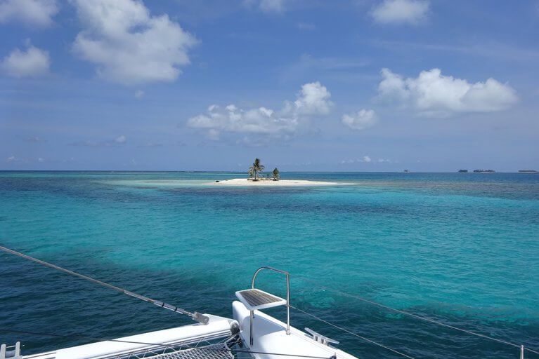View of a small sandy island in the San Blas Islands from the bow of a private catamaran