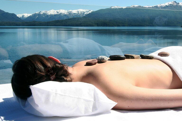 Woman laying down enjoying a luxury spa treatment outdoors with view of snow capped Andes mountains and alpine forest
