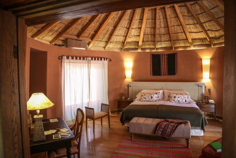 Luxury suite with a large bed, desk, and thatched ceiling at Awasi Hotel in the Atacama Desert