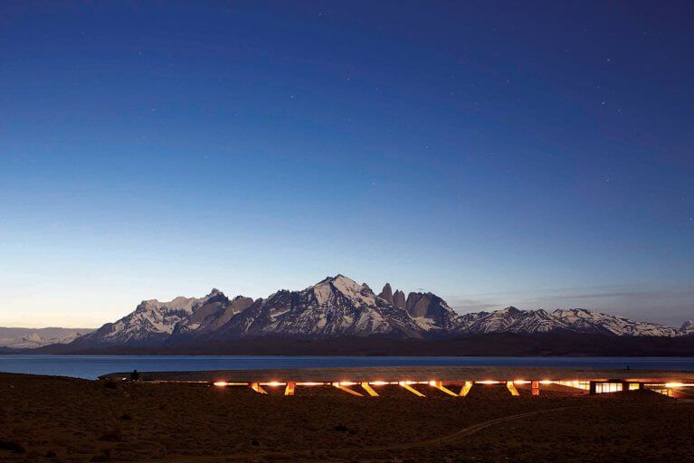 View of the roof and lights of luxury hotel Tierra Patagonia at night with a lake and mountains in the distance
