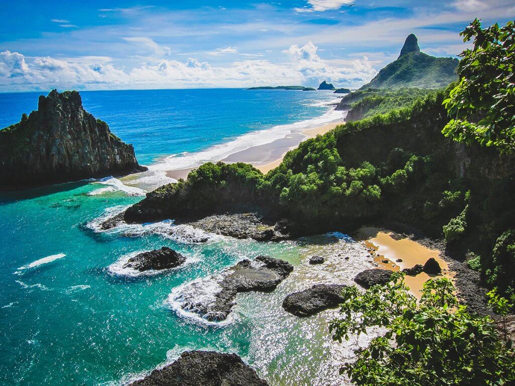 Tropical sea with rocks and a sandy beach with jungle trees in Fernando de Noronha