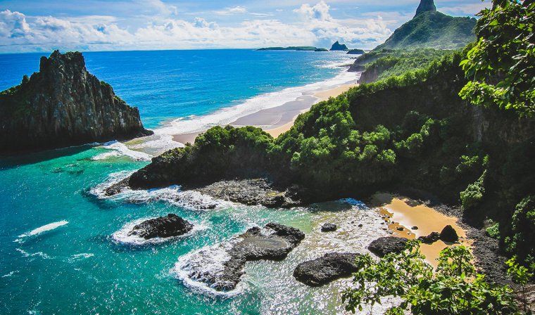 Tropical sea with rocks and a sandy beach with jungle trees in Fernando de Noronha