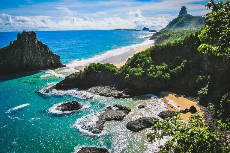 Tropical sea with rocks and a sandy beach with jungle trees in Fernando de Noronha