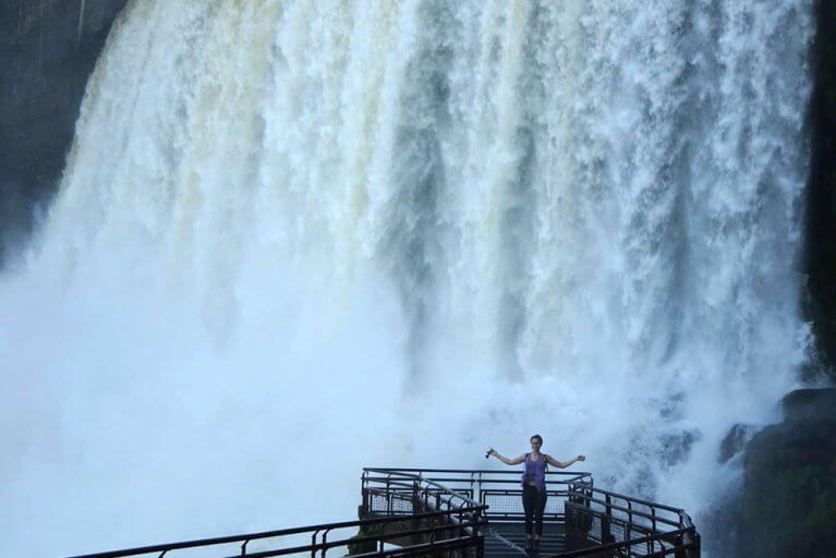 Woman standing on a walkway in front falling water at Iguazu Falls during a luxury tour