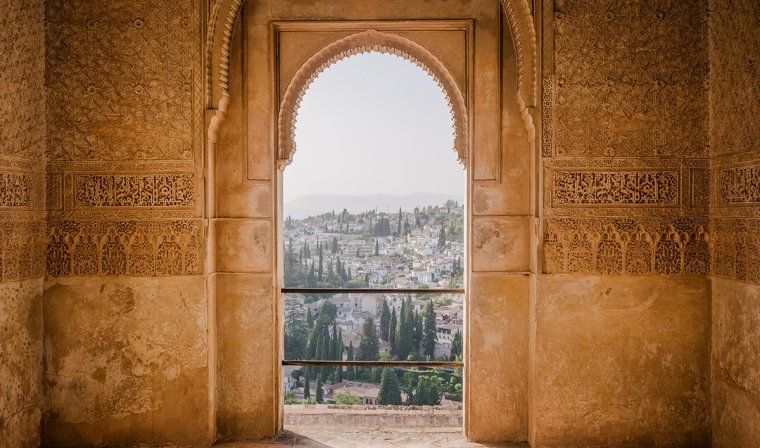 View out of rounded arch window surrounded by intricate Moorish decoration in the Alhambra in Granada, Spain