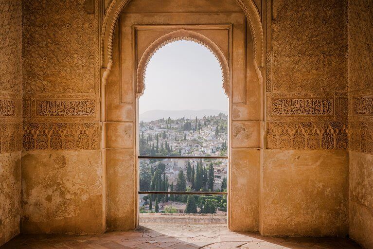 View out of rounded arch window surrounded by intricate Moorish decoration in the Alhambra in Granada, Spain