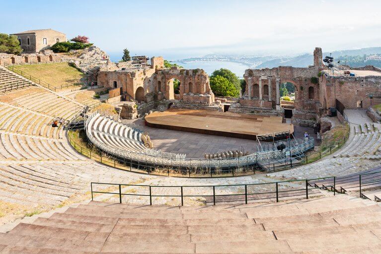 Looking down at stage from top row of ancient Greek amphitheater with a view of the sea in Taormina, Sicily