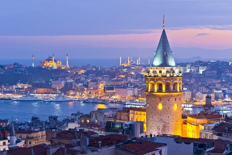 Galata Tower lit up at night with view of Bosphorus River and European side of Istanbul