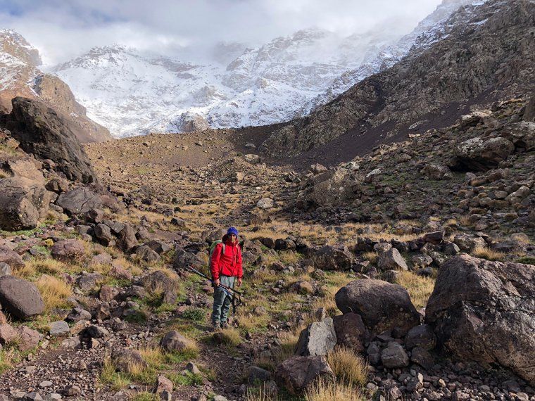 Man in a red jacket during a hiking excursion in Toubkal National Park, with snowy peak behind him