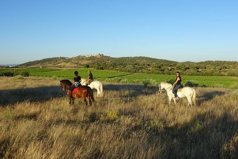 Three people horseback riding in Alentejan countryside with village in background