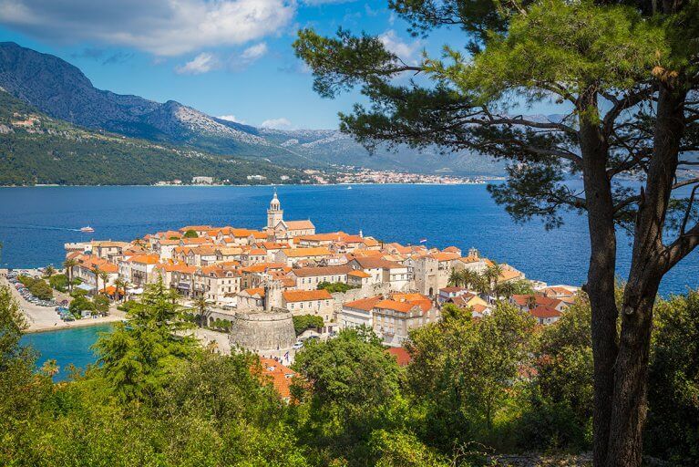 Korčula Old Town seen from forested hillside with Adriatic sea and mountains in background