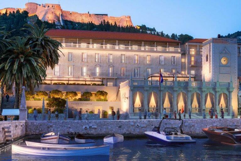 Facade of luxury hotel Palace Elizabeth seen from Hvar harbor with Hvar fortress in distance