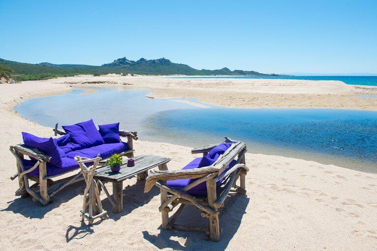 Driftwood sofas with cushions on private beach in Corsica