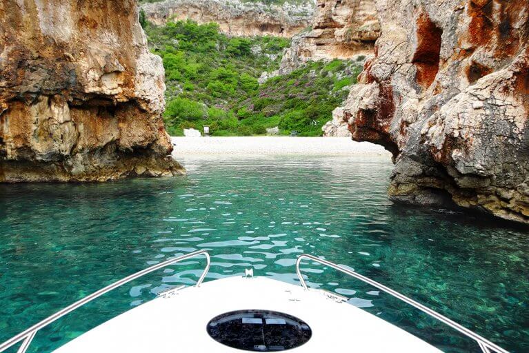 Beach and blue sea between narrow rocky cliffs seen from the bow of a boat during private Adriatic tour