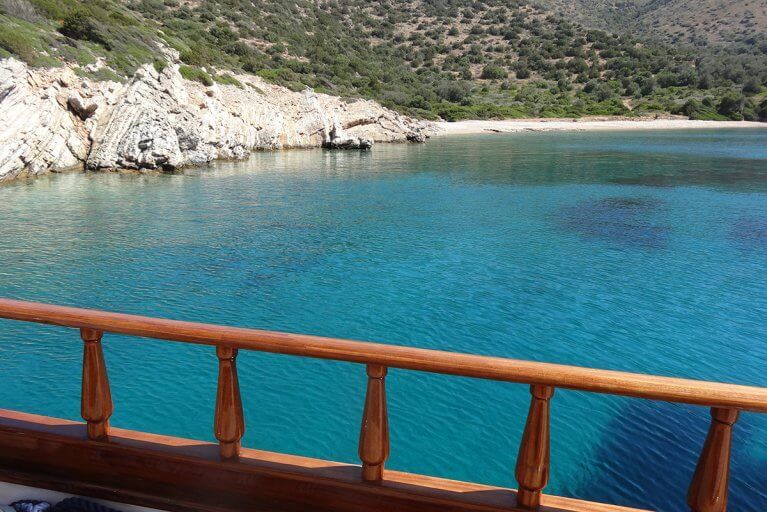 Looking out at rocky coast and blue water over the railing of a traditional Turkish gulet