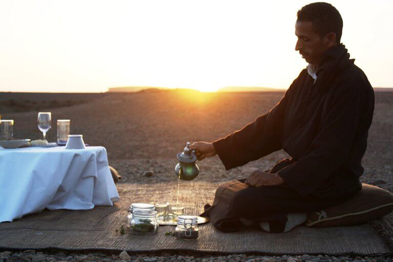 Man pouring a mint tea at sunset in a desert landscape