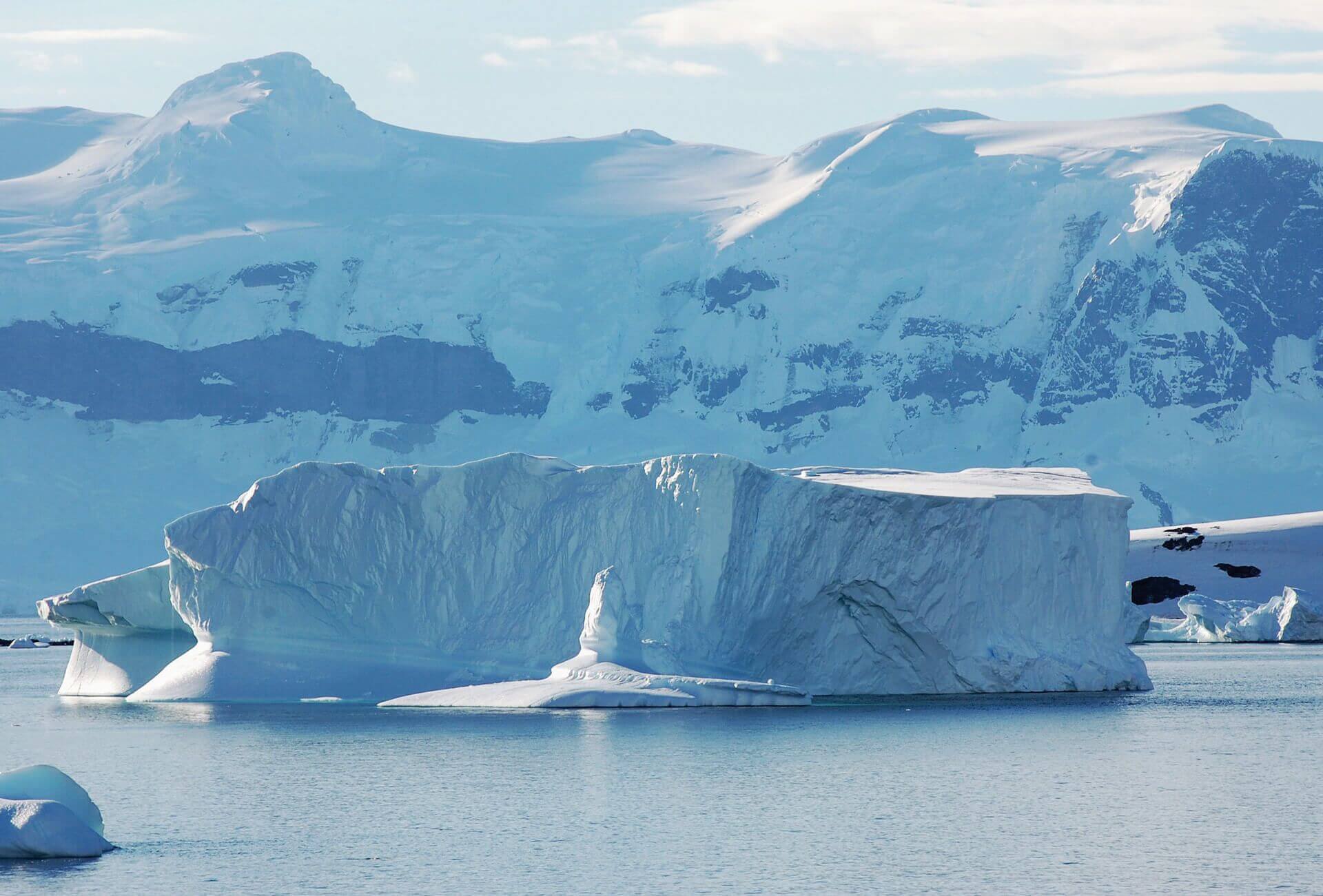 View of enormous iceberg in Antarctica with snow covered mountains in the background