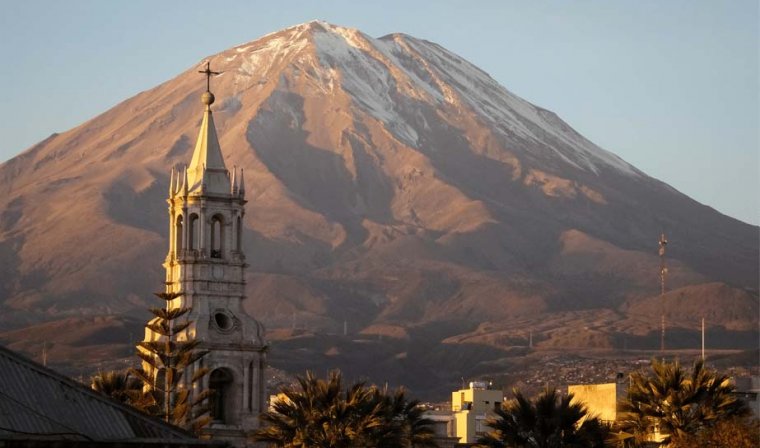 Cathedral spire and palm trees in Arequipa in front of snow capped Misti Mountain in late afternoon light
