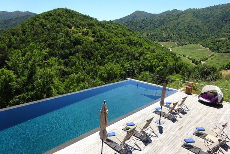 Outdoor pool with a large deck and view of green mountains at Viña Vik hotel in Chile