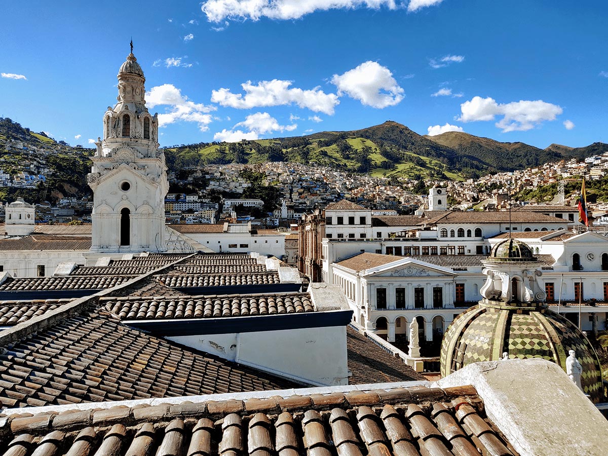 Spire and tiled roof of church with background of houses and green mountains in Quito, Ecuador