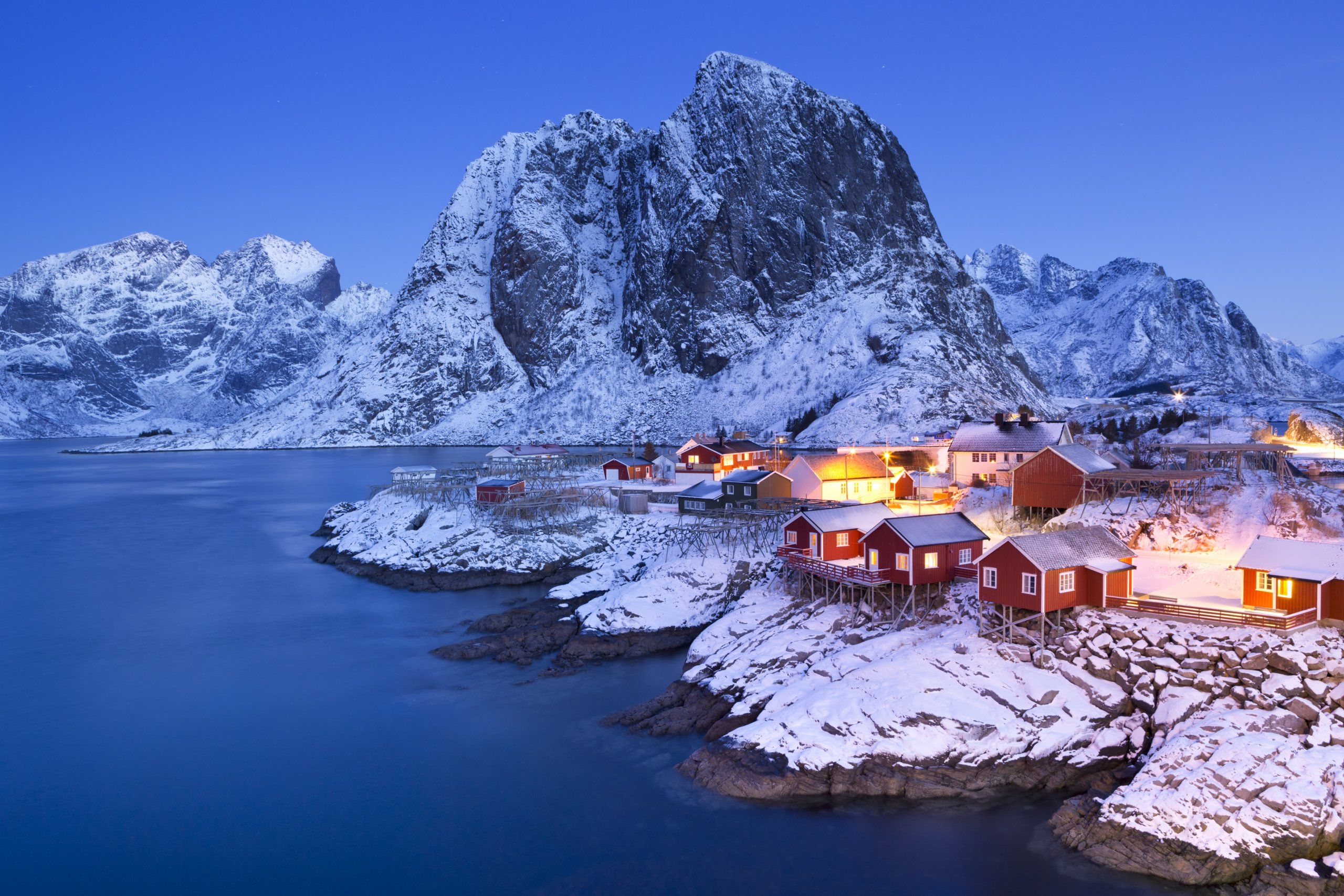 Fisherman's cabins perched on the shore in Lofoten at dusk, with snowy peaks in the background