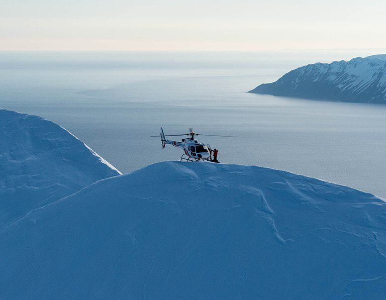 Helicopter hovering above snowy mountains and inlets of Iceland