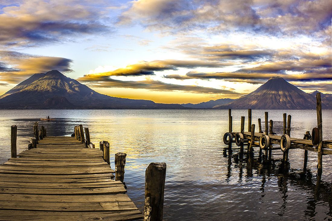 Landscape featuring a dock leading into Lake Atitlan at sunset, with volcanoes in the distance