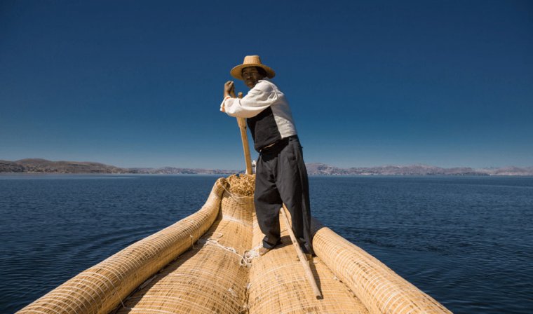 Indigenous man wearing a straw hat steering a large reed boat on Lake Titicaca